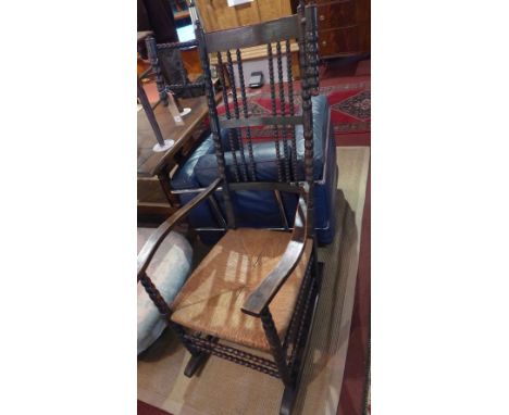 An Ernest Gimson black stained ash and beech rocking chair, with bobbin turned wings and finials, linked by conforming stretc