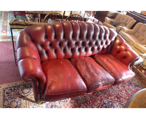 A 20th Century red leather hump back chesterfield three seater sofa raised on turned legs and castors.