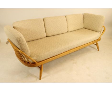 AN ERCOL BEECH AND ELM STUDIO COUCH of rounded oblong form with raised solid back and hooped ends on spindle supports, raised