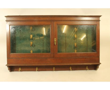 AN ARMY & NAVY OAK BRACKET GUN CABINET, early 20th century, with moulded cornice over two glazed doors opening to baize inter