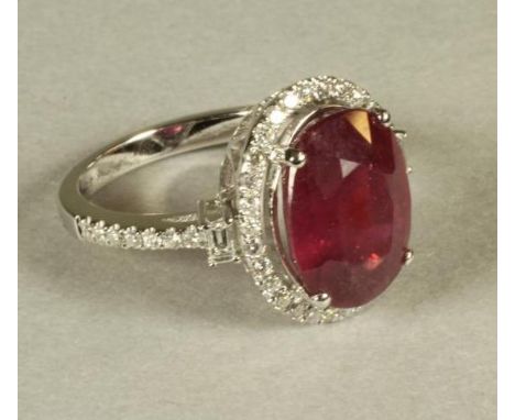 A RUBY AND DIAMOND CLUSTER RING, the oval cut ruby of approximately 6.80cts, claw set to a border of pave set small diamonds,