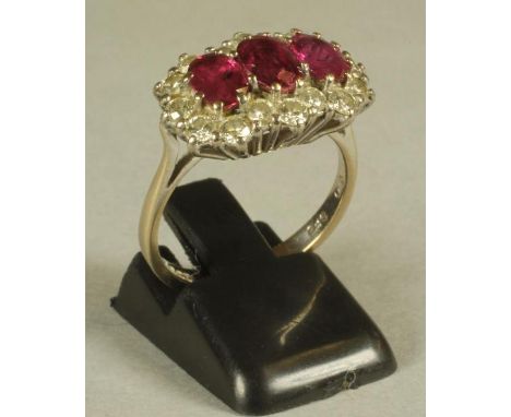 A RUBY AND DIAMOND TRIPLE CLUSTER RING, the three oval cut rubies claw set to a shaped border of small brilliant cut diamonds