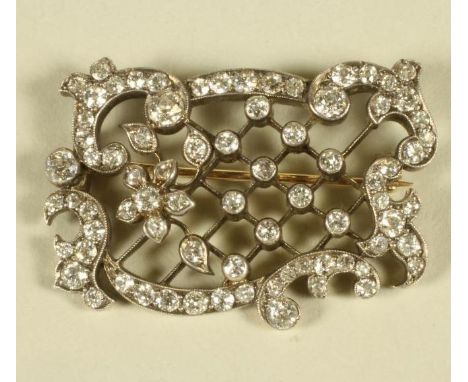 AN EDWARDIAN DIAMOND SET OPEN TRELLIS WORK PANEL BROOCH of rococo form, pave and open back collet set with numerous mix cut s