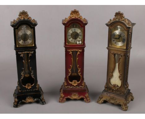 Three miniature grandfather alarm clocks. (33cm high)  Hinge on black clock broken. Catch on back of red clock missing.