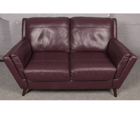 A plum leather two seat sofa raised on small wooden feet. Bought new just several months ago