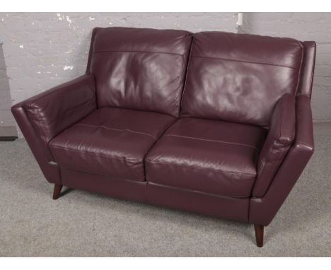 A plum leather two seat sofa raised on small wooden feet. Bought new several months ago