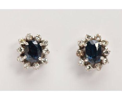 A PAIR OF SAPPHIRE AND DIAMOND CLUSTER EARRINGS, oval cut sapphires assessed as synthetic, set within a surrounding of ten ro