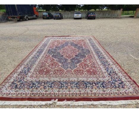 Large carpet with brown edge, geometric patterned with floral decoration, in blues, fawns & red, 315 x 436 cm