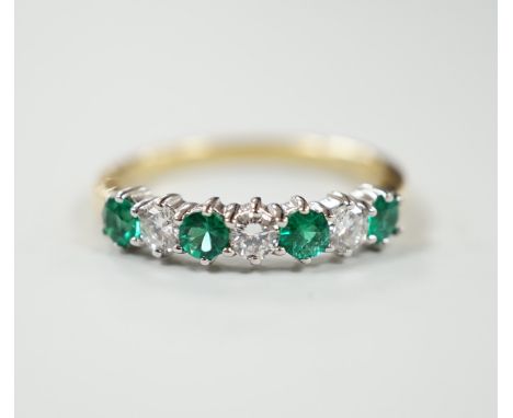 A modern 18ct gold, four stone emerald and three stone diamond set half hoop ring, size M, gross weight 2.9 grams.