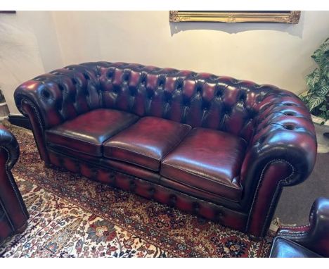 A three-seater leather button back Chesterfield burgundy sofa with metal braid detail on arms and bun feet, manufactured by M