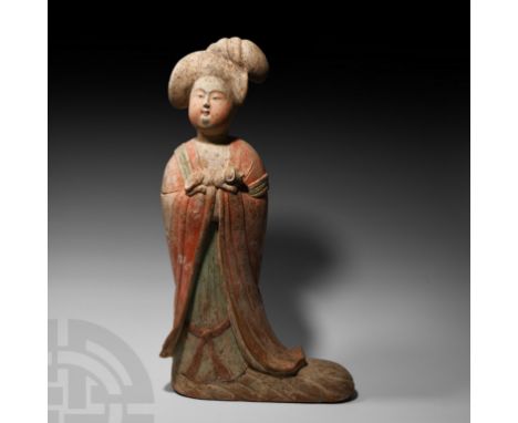 Tang Dynasty, 618-907 A.D. A ceramic figure of a standing lady in floor-length courtly dress with hands enfolded within the s