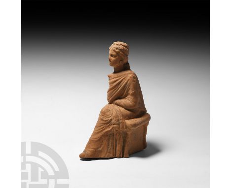 3rd century B.C. A terracotta female figure modelled seated, wearing a full-length robe, one shoe emerging from beneath the h