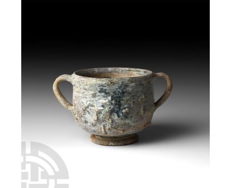 1st century B.C.-1st century A.D. A terracotta skyphos or drinking cup with two ribbed loop handles, rolled foot and appliqué