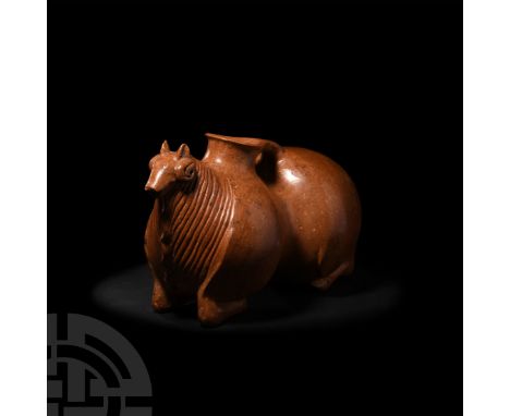 1st millennium B.C. A ceramic rhyton formed as a stylised kneeling ram with figure of eight-shaped body, its slender legs tuc
