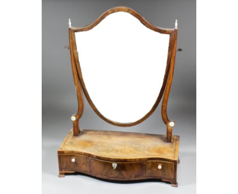 A George III mahogany framed shield shaped toilet mirror on shaped uprights, the serpentine fronted base fitted three drawers