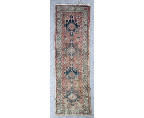 An antique Hamadan runner woven in muted colours with four star shaped medallions on a madder ground, 8ft x 2ft 6ins (extensi