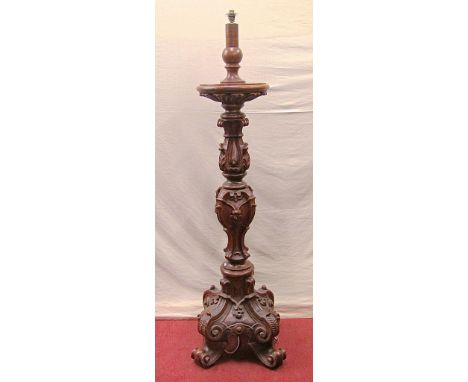 A substantial oak torchere, the column of shaped form, fully carved with acanthus and other geometric detail, raised on scrol