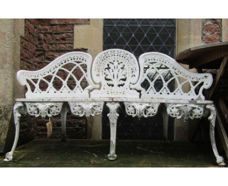 A cream painted cast aluminium garden bench with shaped outline and decorative pierced foliate lattice and geometric detail a