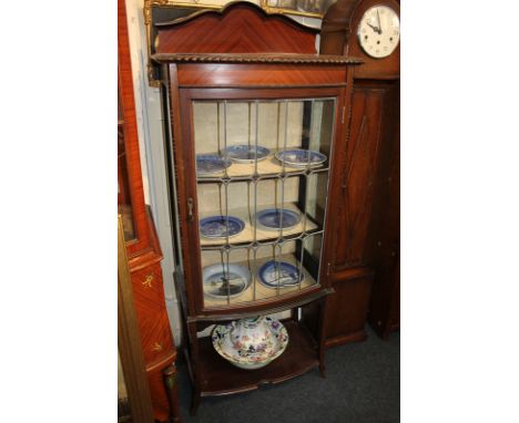 An Edwardian mahogany bow front display cabinet with single lead glazed door enclosing shelves, on curved legs with platform 