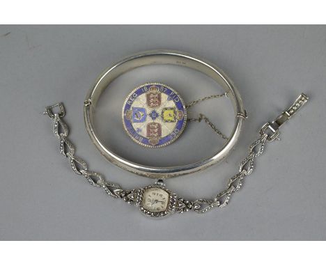 A 20TH CENTURY HINGED SILVER BANGLE, with foliate scroll decoration, together with an enamelled 1887 coin brooch and a ladies