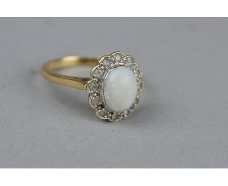 AN OPAL AND DIAMOND 9CT YELLOW GOLD CLUSTER RING, the central oval cabochon cut opal measuring approximately 8mm x 7mm, twelv