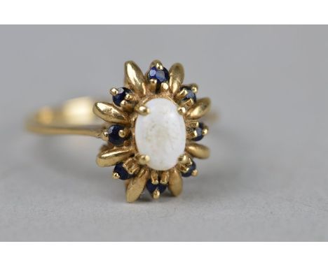 AN OPAL AND SAPPHIRE FANCY OVAL CLUSTER 9CT YELLOW DRESS RING, the four claw set central oval cabochon cut opal with eight sm