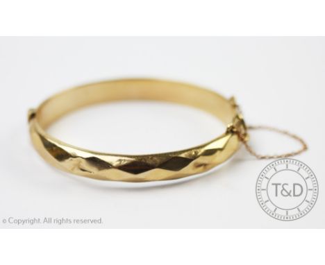 A 9ct yellow gold hinged bangle, Smith and Pepper Birmingham 1963, with faceted detail and safety chain, gross weight 12.5gms