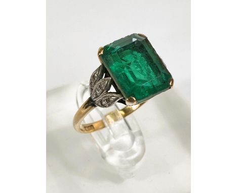 A yellow metal dress ring stamped '18ct' set with large cushion cut emerald doublet with 3 leaf shaped shoulder supports to e