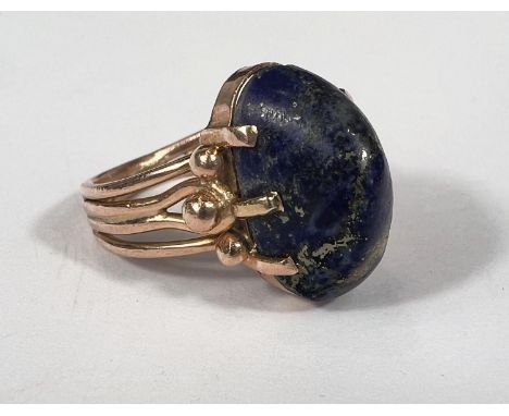 A lapis lazuli stone dress ring held by 3 yellow metal claws to each shoulder, the shank formed from 4 separate yellow metal 