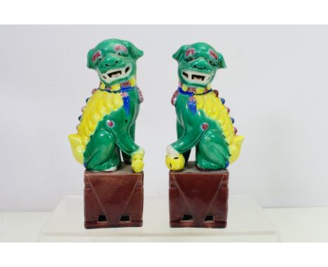 A pair of Chinese Buddhist Lion figures, each modelled in mirror image seated on stands with open mouths, approximately 21 cm