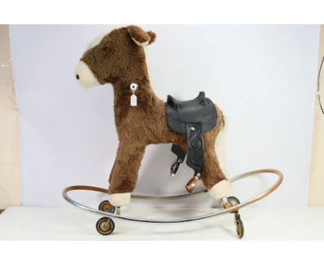 An unmarked plush rocking horse, mounted on metal frame with wheels. The brown horse with white mane, black saddle has age an