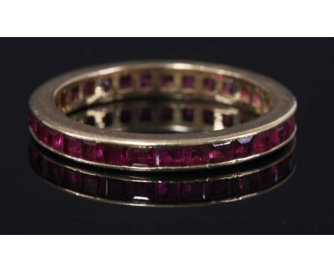 A gold ruby flat section full eternity ring,with a series of calibré cut rubies, all channel set to plain guards. Tested as a