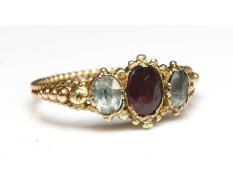 An early Victorian three stone foiled garnet and foiled quartz ring,with an oval mixed cut foiled garnet, claw set to the cen