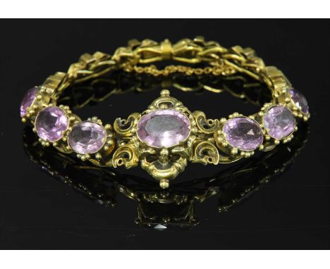 A Victorian gold amethyst bracelet, c.1850,with a scrolling centrepiece, claw set with an oval mixed cut amethyst. A series o