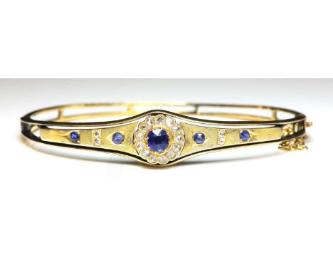 An Edwardian gold sapphire and diamond bangle, c.1900,with a sapphire and diamond cluster centrepiece. A circular Swiss cut s