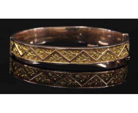 An early 20th century gold hollow hinged bangle,by Smith &amp; Pepper, with raised chevron decoration. Repoussé guards betwee