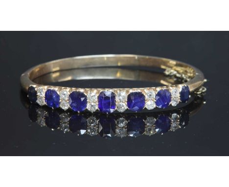 A late Victorian sapphire and diamond hinged bangle, c.1890,with a row of seven graduated cushion-shaped mixed cut sapphires,