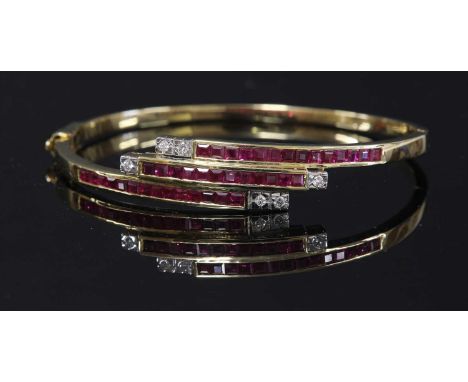 A gold ruby and diamond crossover hinged bangle,with three rows of channel set calibré cut rubies, in diagonal rows. A total 