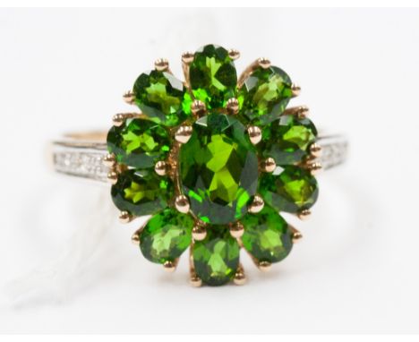 A green garnet cluster ring, set central oval faceted stone within border of ten further garnets, diamonds to the shoulders, 