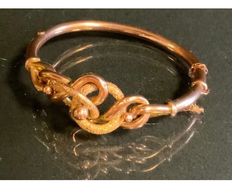A gold coloured metal scroll knot hinge bangle, stamped 9ct, 11.4g gross, cased 