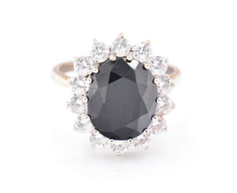 A hallmarked 9ct gold, sapphire and CZ cluster ring. The 9ct gold ring set with a central oval cut sapphire and surrounded by