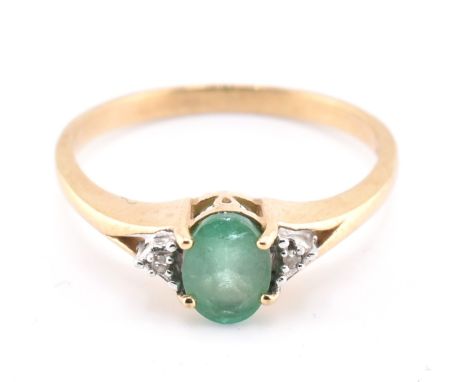 A hallmarked 9ct gold emerald and diamond ring. The 9ct yellow gold ring having a four claw set oval cut emerald flanked to e