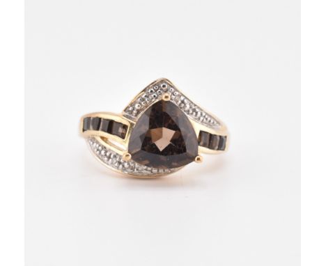 A hallmarked 9ct gold smoky quartz and diamond ring. The 9ct yellow gold ring set with a central trilliant cut smoky quartz w