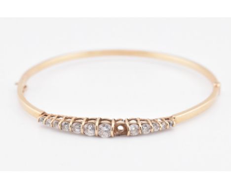 A hallmarked 9ct gold and CZ hinged bangle AF. The 9ct yellow gold hinged bangle set with a single row of bar set graduating 