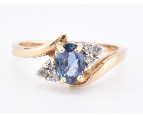 A hallmarked 9ct gold sapphire and diamond crossover ring. The 9ct yellow gold ring set with a central oval cut sapphire flan