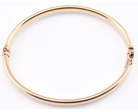 A 9ct gold hinged bangle. The 9ct yellow gold hinged bangle having a concealed box clasp with bracelet catch to top. Marks ru