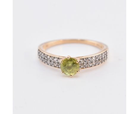 A hallmarked 9ct gold and gem set ring. The 9ct yellow gold ring set with a central six claw set round cut green stone to sho