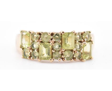 A hallmarked 9ct gold and peridot ring. The 9ct yellow gold ring set with four emerald cut peridots interspersed by thirteen 