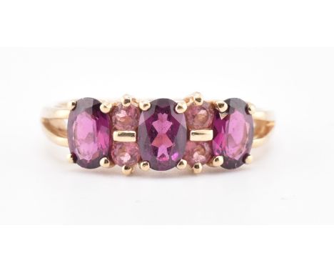 A hallmarked 9ct gold, garnet and tourmaline ring. The 9ct yellow gold ring set with three four claw set oval cut garnets int