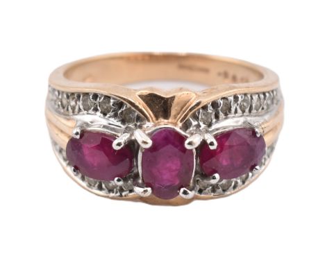 A hallmarked 9ct gold ruby and diamond three stone ring. The ring set with three four claw set oval cut rubies and twenty thr